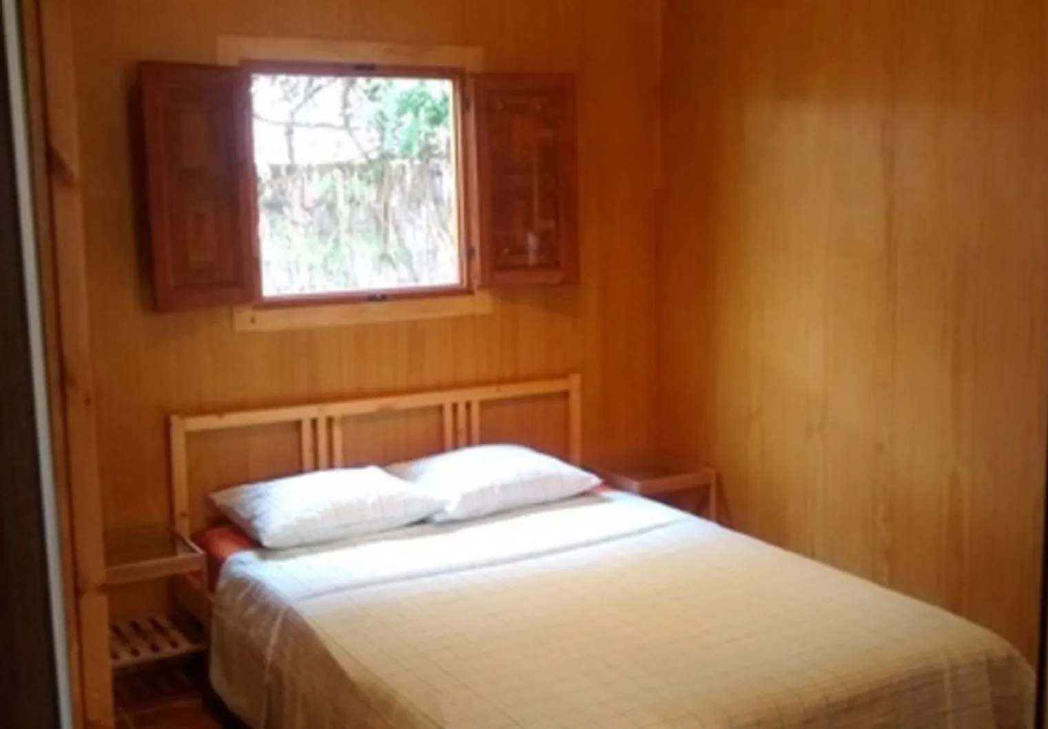 Dormitorio de la casita de madera con cama de matrimonio y ventana al jardín