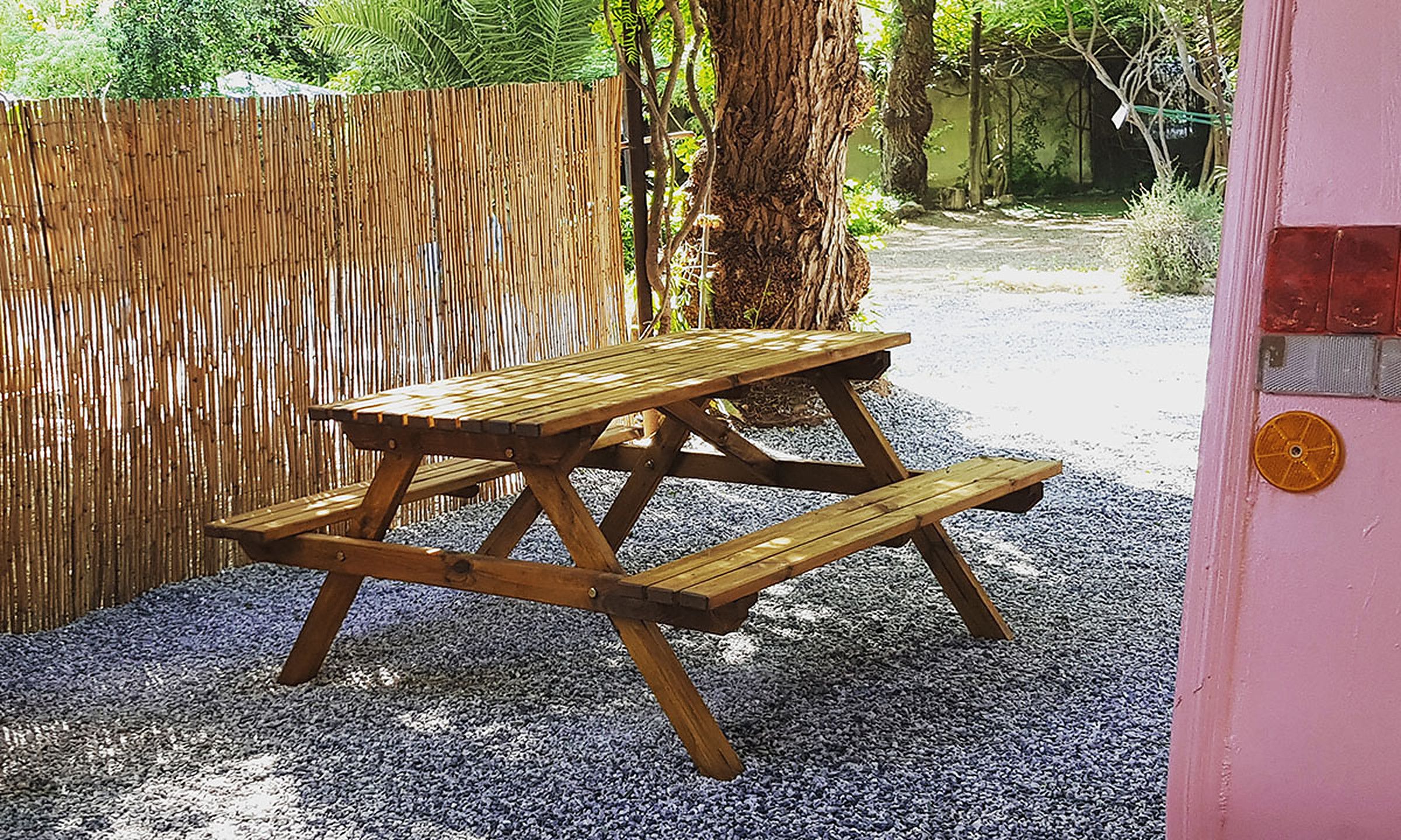 Mesa de merendero de madera junto a una caravana, con cañizo y sombra